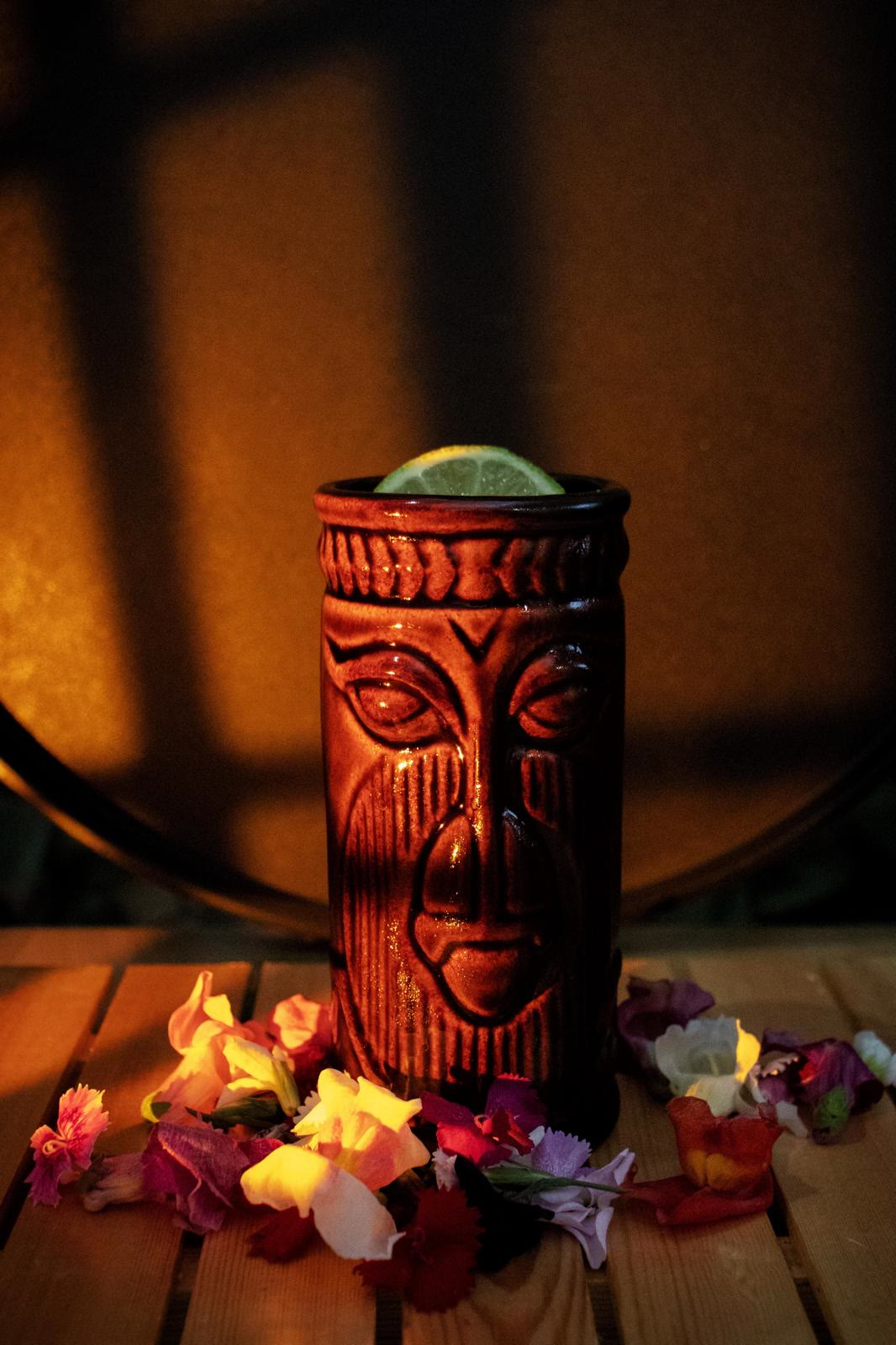 Cóctel tiki con lima sobre mesa de madera y flores