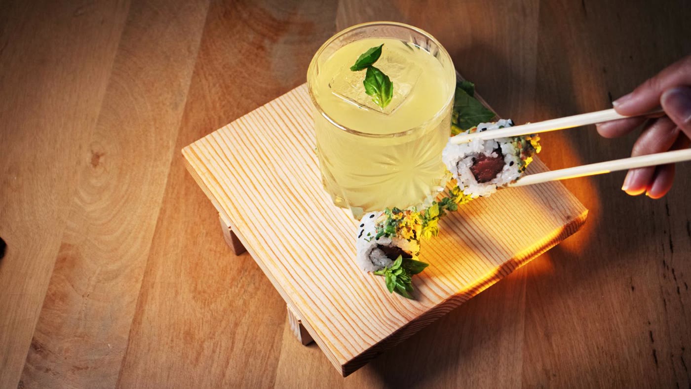 Cóctel con albahaca y sushi sobre tabla de madera