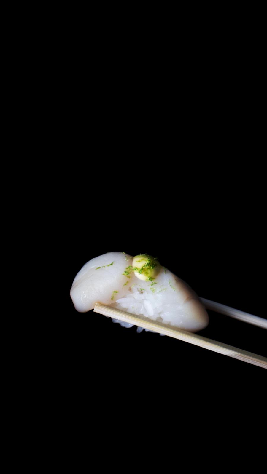 Nigiri de vieira con ralladura de lima sobre fondo negro