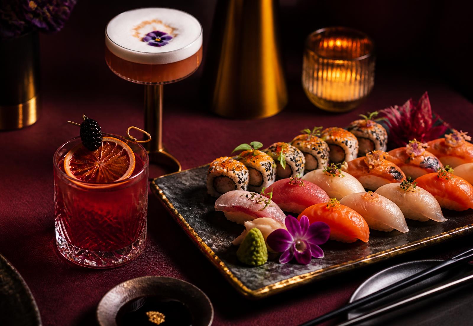 Bandeja de sushi de autor junto a cócteles sobre mantel granate